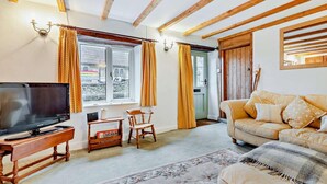 Una sala de estar con televisión, muebles de madera, un sofá, un tapete estampado y una ventana con cortinas.