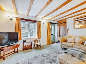 Ein Wohnzimmer mit Fernseher, Holzmöbeln, einer Couch, einem gemusterten Teppich und einem Fenster mit Vorhängen.