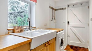Una cocina con lavamanos, armarios de madera, lavadora y ventana con vista a árboles.