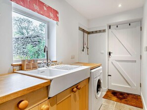 Eine Küche mit Spüle, Holzschränken, einer Waschmaschine und einem Fenster mit Blick auf Bäume.