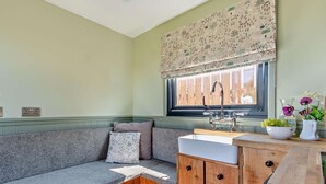 A compact kitchen with a built-in bench, a window with a floral valance, and a sink with a wooden countertop.