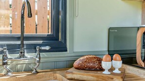 A kitchen with a wooden countertop, a bread loaf, two eggs in egg cups, a sink with a faucet, and a television.