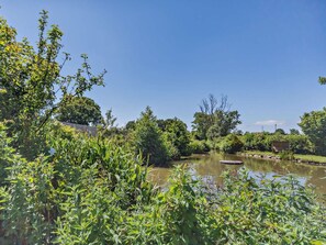 A serene outdoor setting with a pond, lush greenery, and a wooden structure.