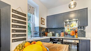 Une cuisine moderne avec des meubles de couleur sombre, un plan de travail en bois, un panier de fruits, un grille-pain vintage et une grande fenêtre.