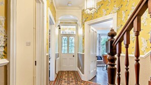 Un couloir doté d’un revêtement de sol à motifs, d’un escalier en bois et d’une porte donnant sur une autre pièce.