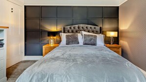 Une chambre à coucher avec un grand lit, une tête de lit sombre, des lampes de chevet et une armoire.