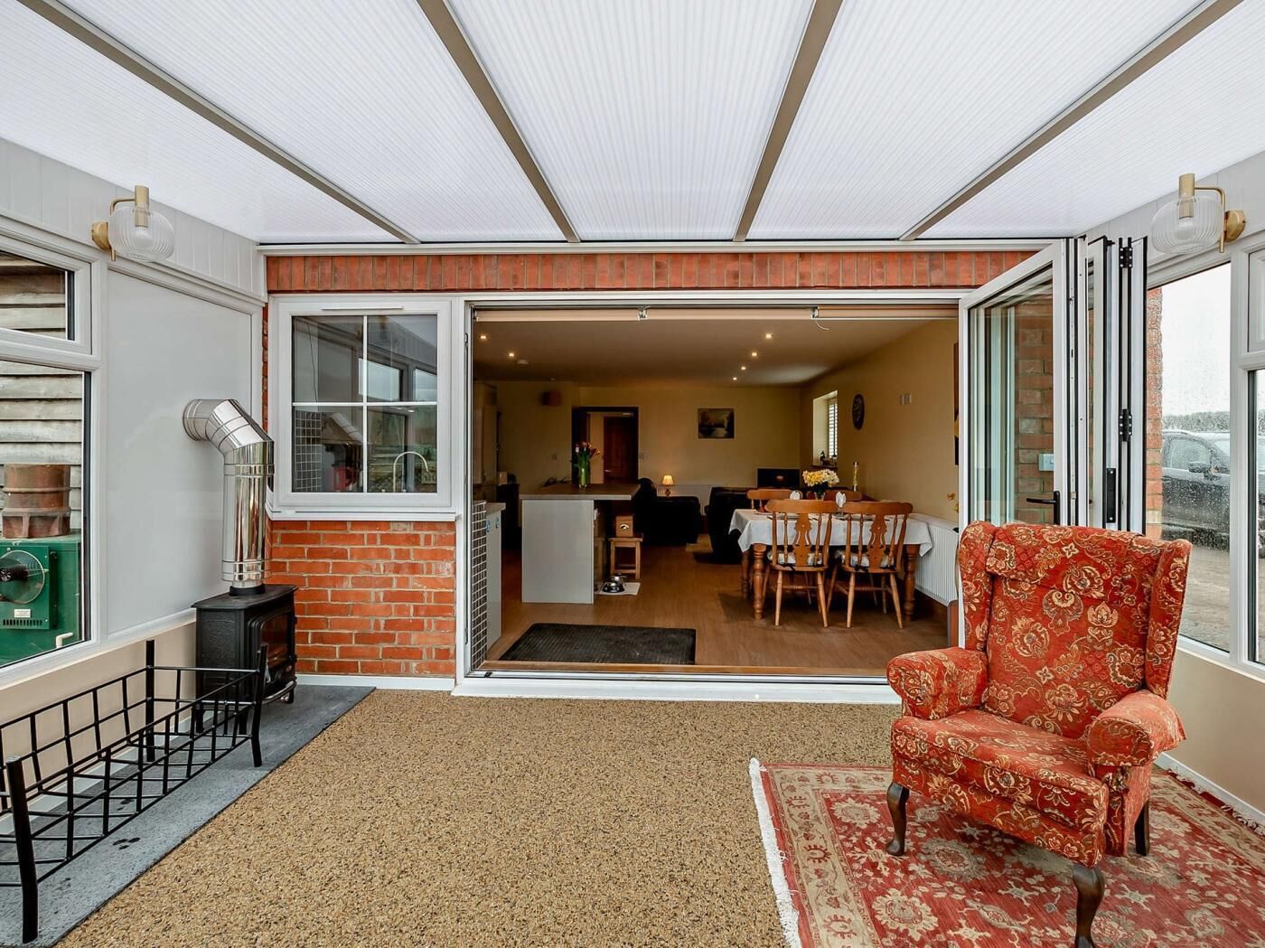 Uma sala de estar acolhedora com uma poltrona vermelha estampada, um espaço de jantar com mesa e cadeiras, e uma cozinha visível por uma porta aberta.