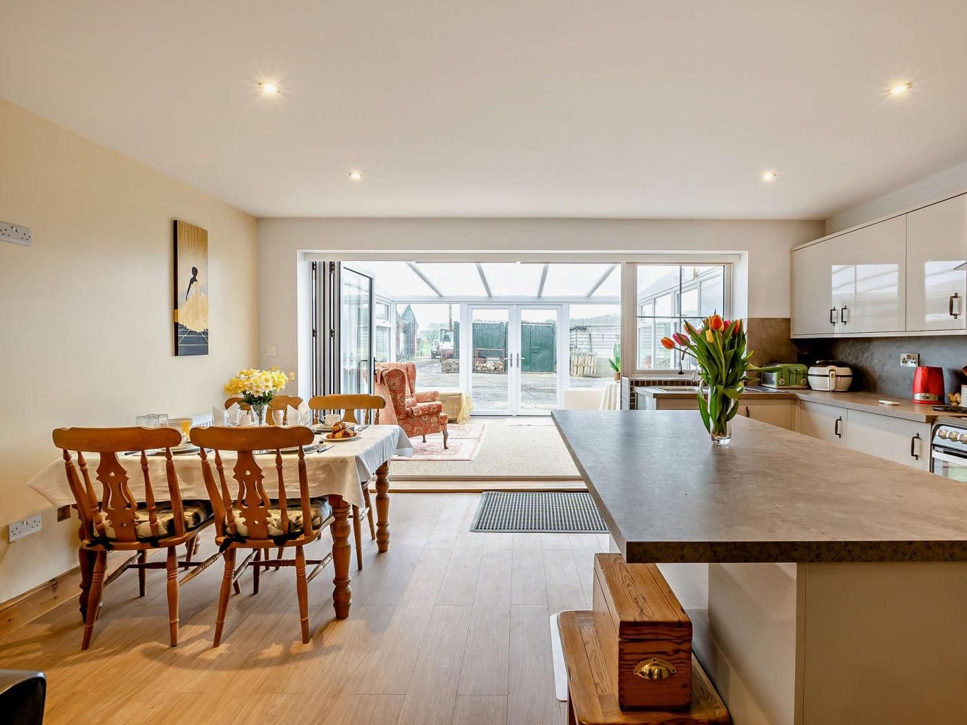 A modern kitchen with a large island, wooden chairs, and a dining table with a vase of flowers.