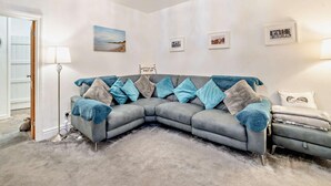 Ein Eckwohnzimmer mit einer grauen Eckcouch, einer Stehlampe und einem an der Wand befestigten Bilderrahmen.