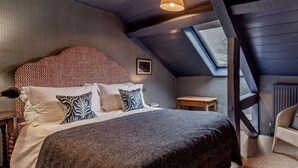 A bedroom with a sloped ceiling, a bed with patterned pillows, a small bedside table, and a view through a skylight. - 8 Bed in Dorchester (oc-93723) (Minterne Magna)