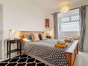 A bedroom with a bed, bedside tables, a desk, a chair, a window, and a hanging light fixture.