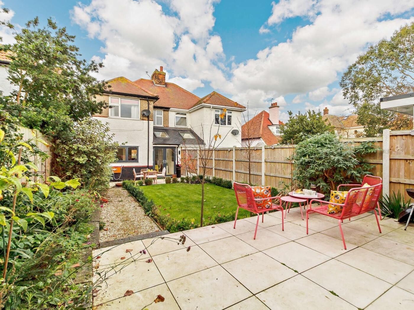 A residential backyard with a patio, chairs, and a small garden.