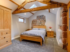 Une chambre avec un lit en bois, un mur en pierre, une petite fenêtre et une armoire en bois.