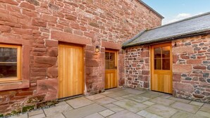 Un bâtiment en pierre doté de deux portes en bois et d’une terrasse carrelée.