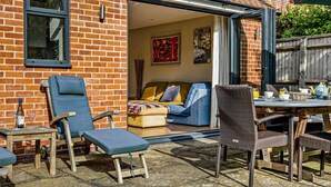 Un patio con mobiliario exterior, una mesa con juego de té y vista a una habitación con sofá y obras de arte.