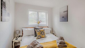 Habitación de hotel con una cama, una mesita de noche, una lámpara, una ventana con persianas y toallas sobre la cama.
