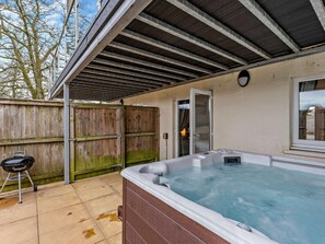 Un jacuzzi en un área exterior techada con cerramiento de madera y una parrilla.