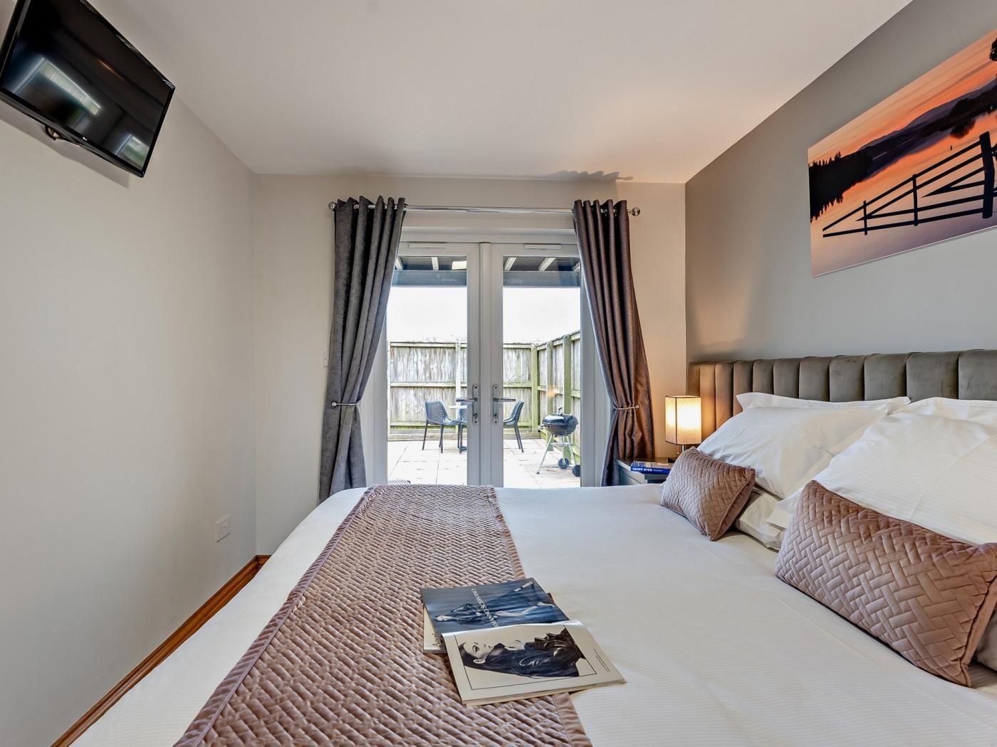 A hotel room with a bed, a TV mounted on the wall, and a view of the outside.