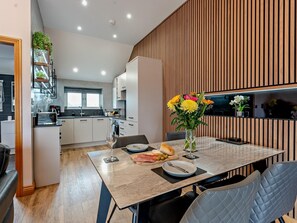 Una cocina moderna con armarios blancos, una zona de comedor con mesa de mármol y una pared decorativa de madera.