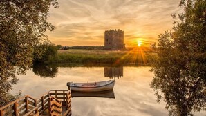 A calm river with a wooden dock, a boat, and a castle in the background during sunset.
