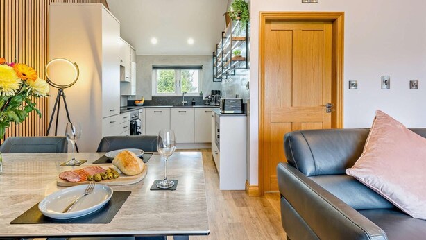 A modern kitchen with a dining area, a sofa, and a door.
