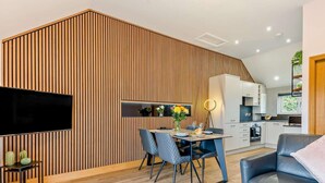 A modern living room with a dining area, a kitchen, and a TV mounted on a wooden wall.