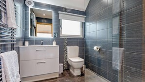 A modern bathroom with a glass shower enclosure, a white vanity, and a dark tiled wall.