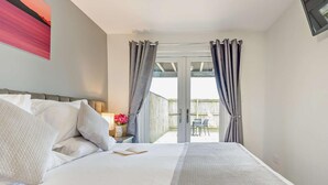 A bedroom with a bed, curtains, a nightstand, a lamp, and a view of an outdoor patio.