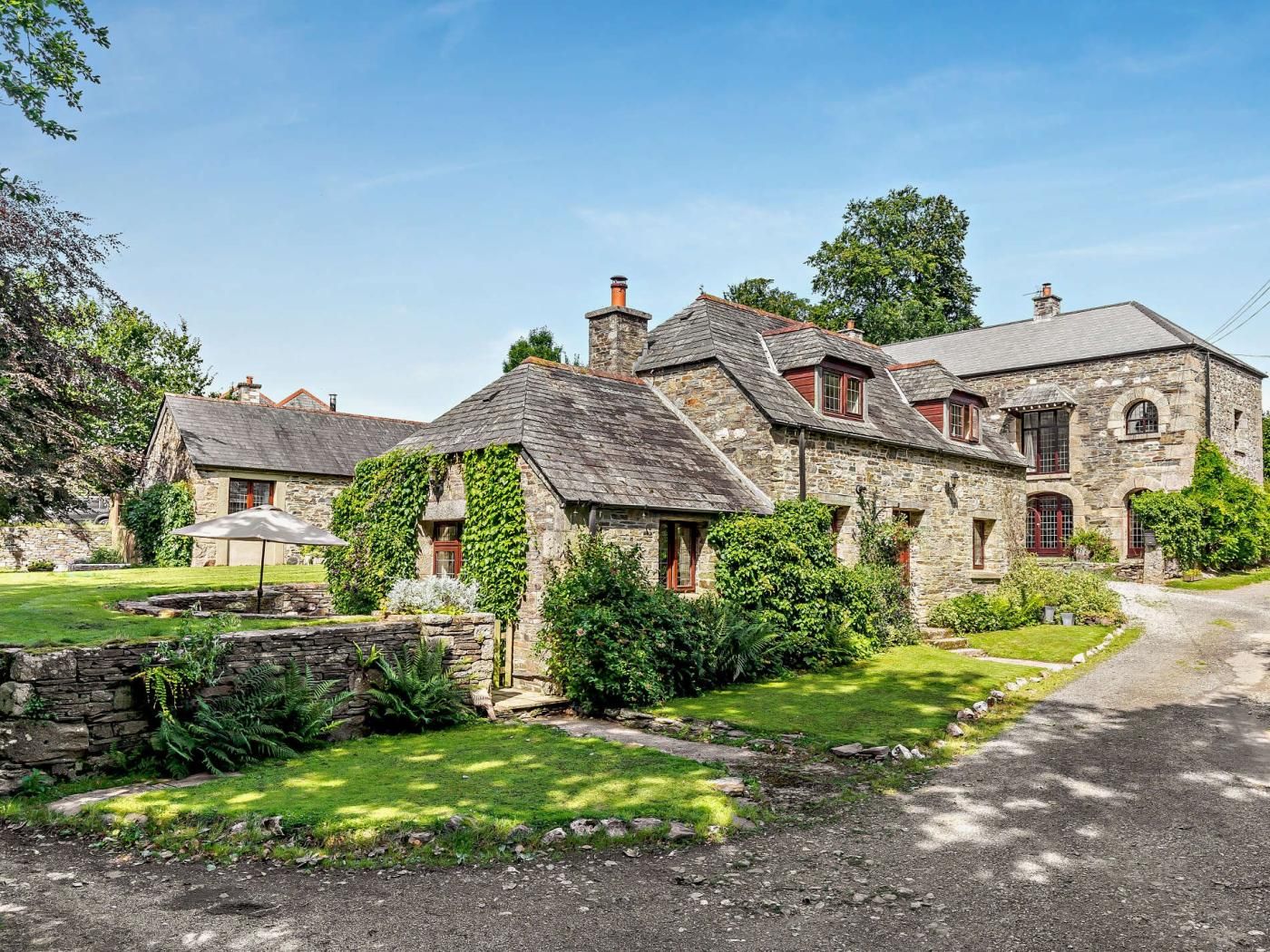 A stone house with a garden, a stone wall, and a gravel driveway.