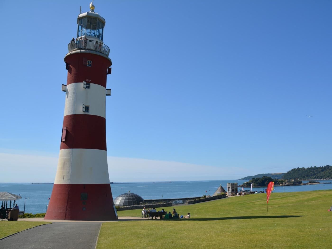 A lighthouse with a clear sky, a grassy area, and a body of water in the background.