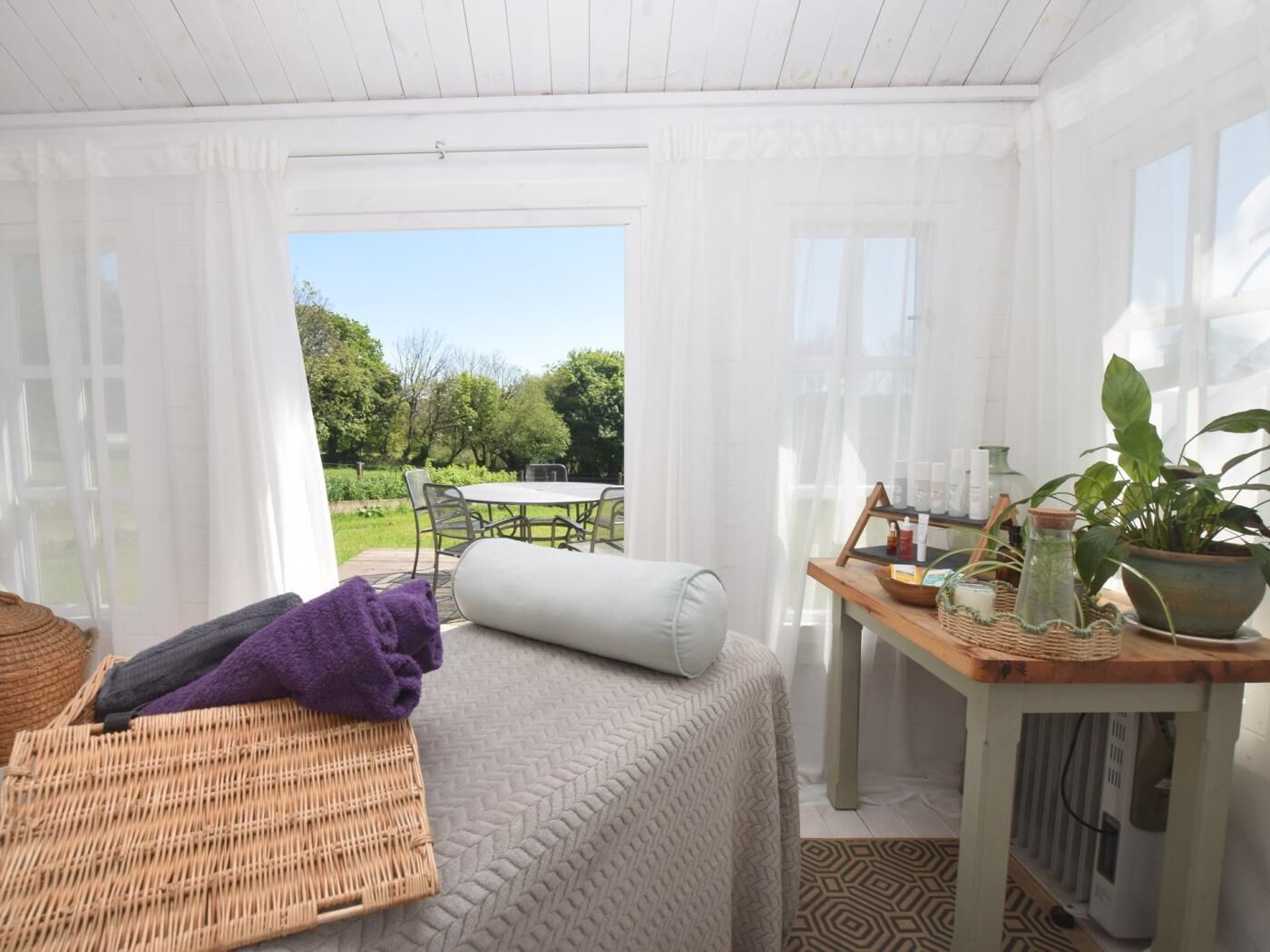 Ein gemütliches Zimmer mit einem Bett, einem Korbwäscheschrank, einem kleinen Tisch mit Toilettenartikeln und Blick ins Freie.