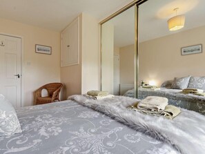 Quarto com um espelho grande, uma cadeira de vime, uma cama com colcha estampada e uma mesa de cabeceira com abajur.