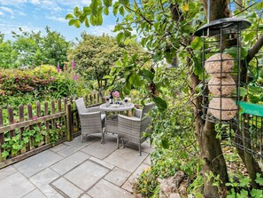 Eine Terrasse mit Korbmöbeln, einem runden Tisch und einem Holzzaun.