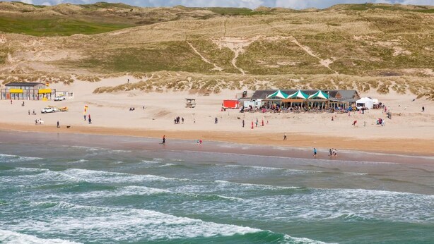 Een strand met een gebouw en tenten, een zandstrand en golven.