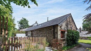 A stone building with a sloped roof, a wooden fence, and a garden with various plants. - 2 Bed in Callington (oc-tyler) (South Hill)