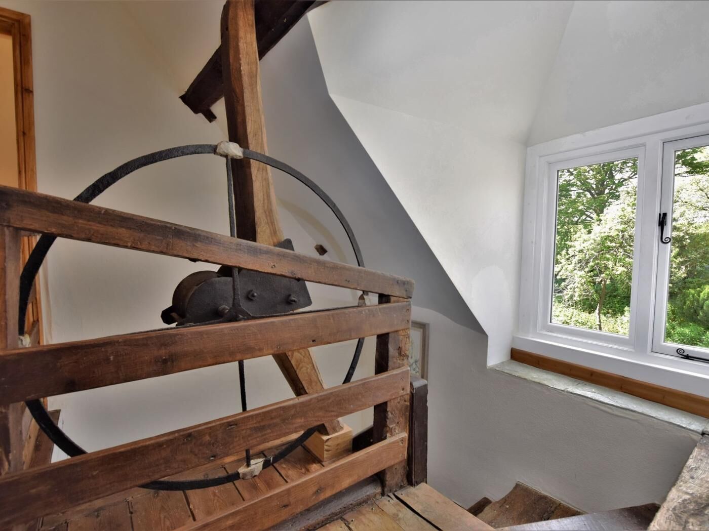 Um quarto com teto inclinado, janela com vista para o verde e estrutura de madeira com sistema de polia.