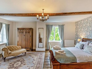 A bedroom with a large bed, a chaise lounge, a wooden wardrobe, a mirror, and a chandelier.