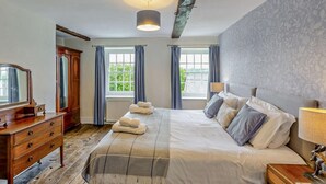 Et soveværelse med seng, kommode, spejl, et vindue med gardiner og en lampe.