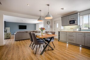 A modern kitchen with grey cabinets, a wooden dining table, and a grey sofa in the living area. - 2 Bed in Weymouth (oc-75200) (Weymouth)