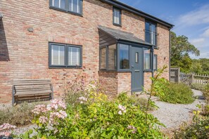 A brick house with a grey door, a bench, and a garden with flowers. - 2 Bed in Weymouth (oc-75200) (Weymouth)