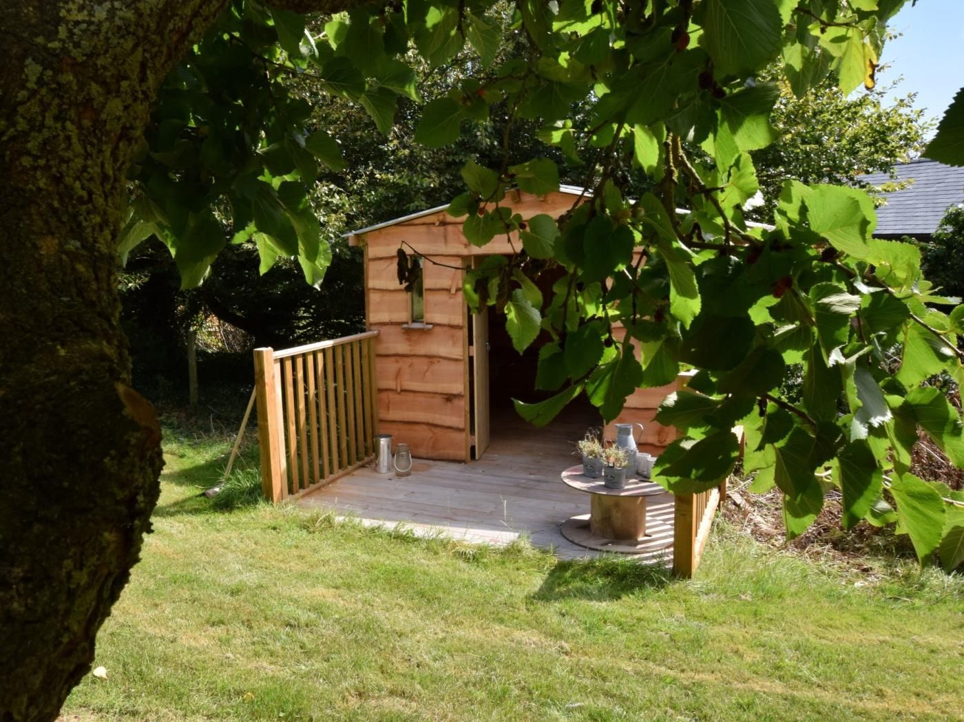 Une cabane en bois dotée d’une terrasse, entourée d’herbe et d’arbres.