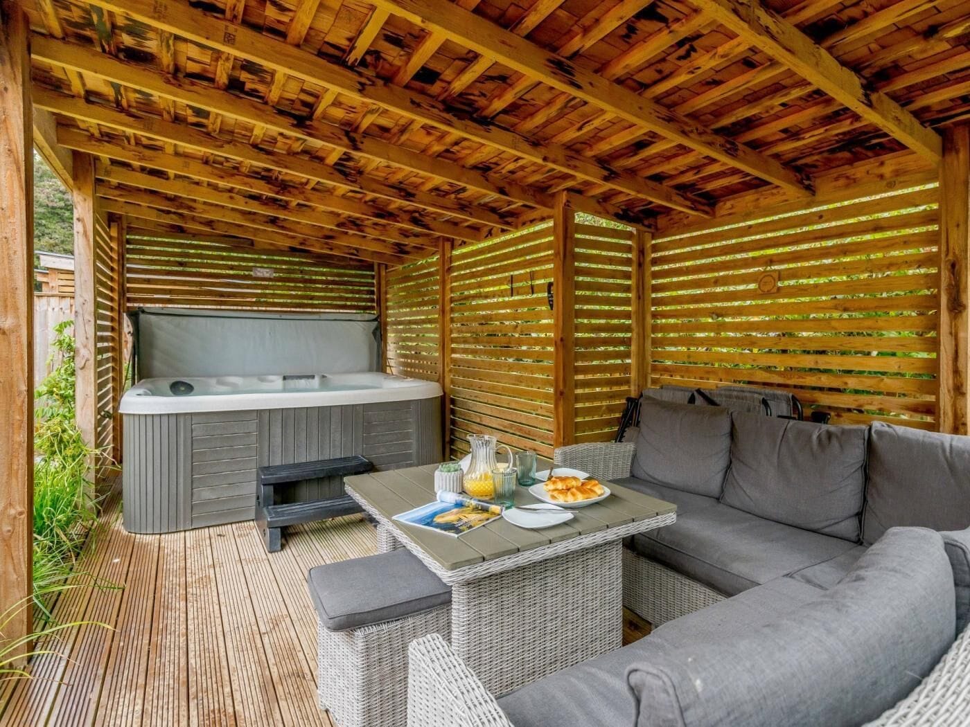 An outdoor patio with a hot tub, wicker furniture, and a wooden ceiling.