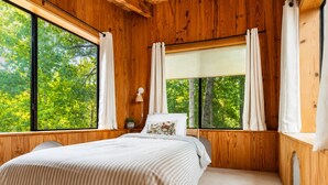 A wooden room with a bed, large windows, and a view of trees.