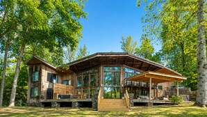 A wooden cabin with large windows, a covered porch, and a stone foundation.
