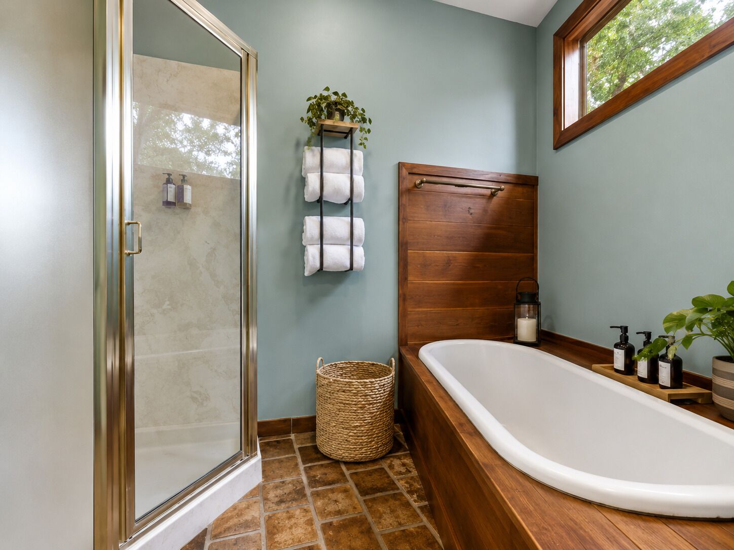 A bathroom with a glass shower enclosure, a wooden bathtub, a towel rack with towels, a wicker basket, and a potted plant.