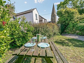 Een houten picknicktafel buiten, compleet met borden en glazen, omringd door groen en een kerktoren in de verte.