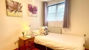 Un dormitorio con cama, mesita de noche, lámpara y dos cuadros de flores colgados en la pared.