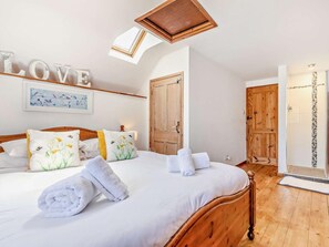 Een slaapkamer met een bed, dakraam, een houten kledingkast en een douchegedeelte.