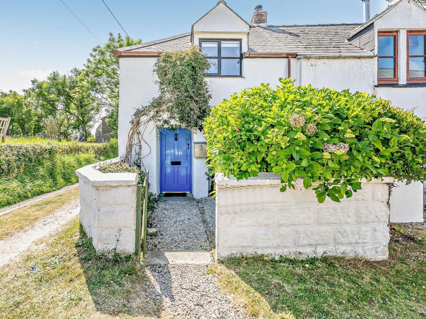 Uma casa com porta azul, um caminho de cascalho até a entrada e um jardim com arbustos verdes.
