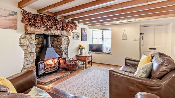 Una sala de estar acogedora con chimenea de piedra, vigas de madera, mobiliario de cuero y televisor.